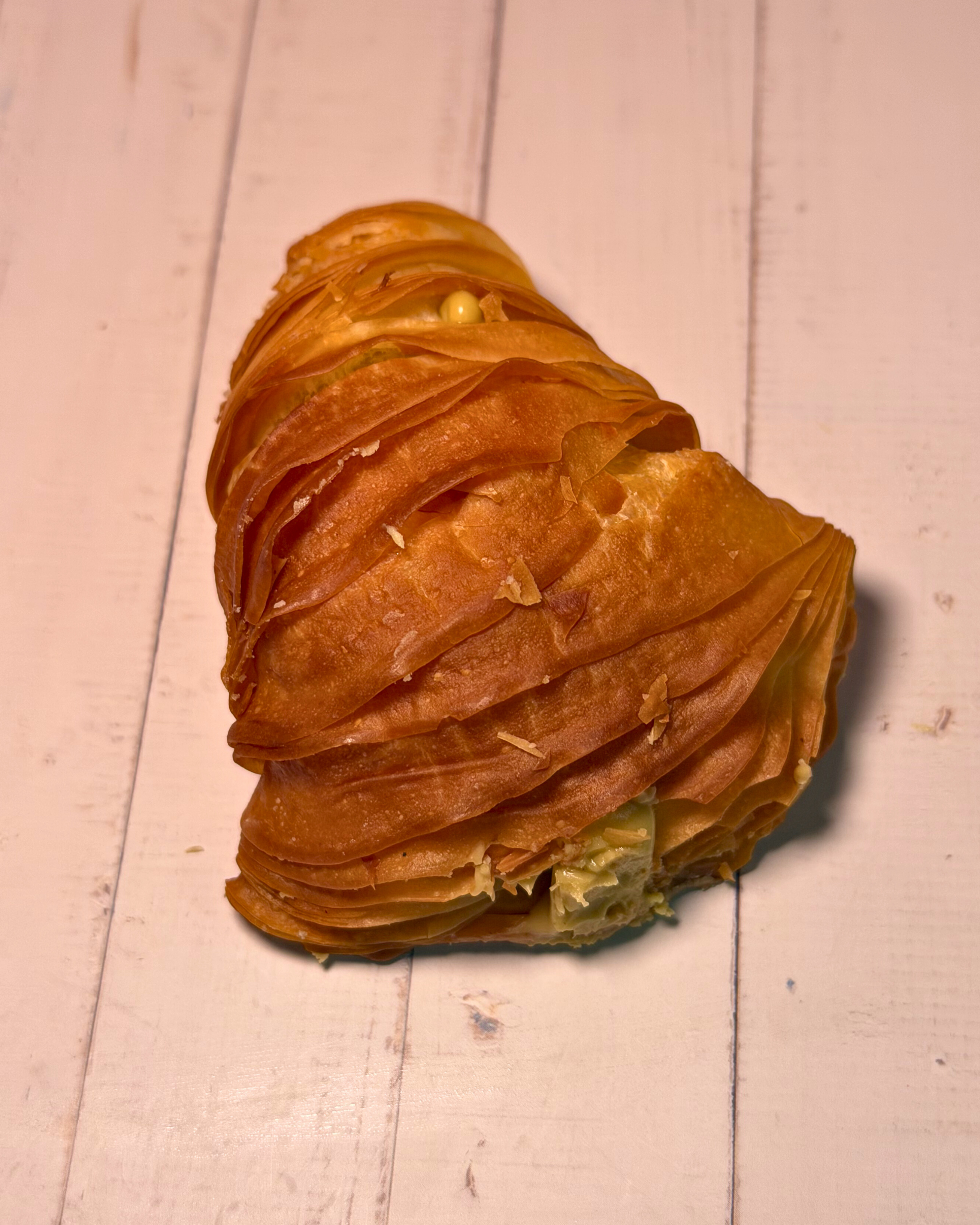 Medri pistachio sfogliatella de pastry with golden, flaky layers and pistachio filling, showcased on a white plate.